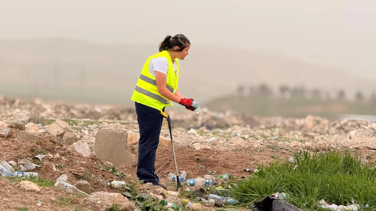 A woman in a high-visibility vest picking up litter.